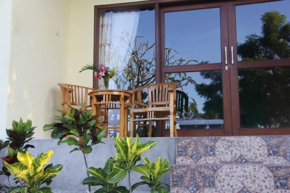 A patio area with a wooden table and chairs, surrounded by potted plants and a tiled wall.