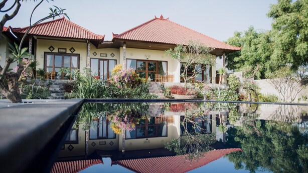 A two-story house with a red-tiled roof, large windows, and a reflection in the water. - Segara Tegeh - Hostel (Tulamben)