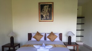 A neatly made bed with a white comforter and two brown pillows, flanked by two bedside tables with lamps, in a room with a framed artwork above the bed. - Segara Tegeh - Hostel (Tulamben)
