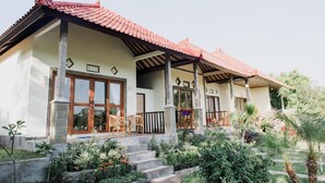 A two-story house with a tiled roof, large windows, and a garden with various plants and a staircase leading to the entrance. - Segara Tegeh - Hostel (Tulamben)