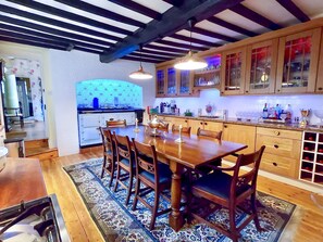 A spacious kitchen with a wooden dining table and chairs, a built-in oven, and wooden cabinets with glass doors. - River Nene Cottages (Peterborough)