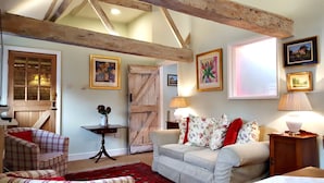 A cozy living room with exposed wooden beams, a plaid sofa, a floral-patterned armchair, and a red rug. - River Nene Cottages (Peterborough)