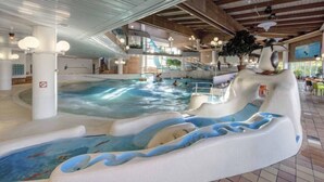 An indoor water park with a wave pool, slides, and a seating area with a large tree. - Hotell Kringelstaden (Sodertalje)