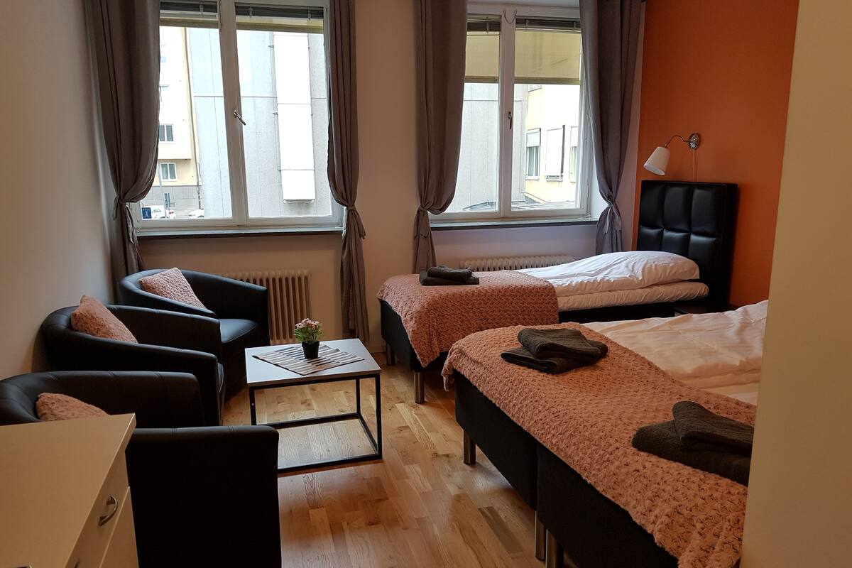 Ein Hotelzimmer mit zwei Betten, einem Schreibtisch, einem Stuhl und einem fenster mit Vorhängen.