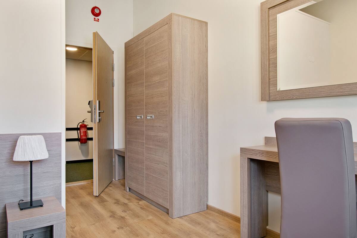 Ein Hotelzimmer mit Holzschrank, Schreibtisch, Stuhl, Lampe und Feuerlöscher.