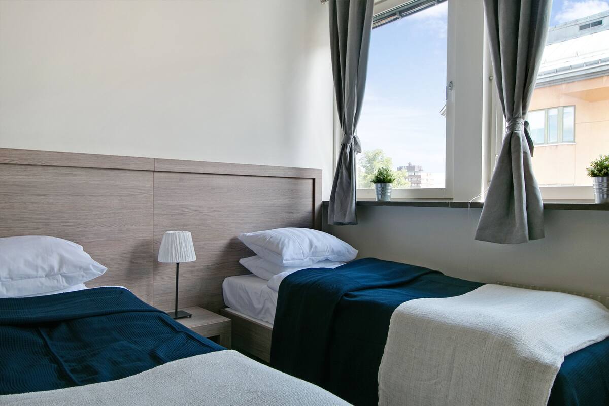 Ein Hotelzimmer mit zwei Betten, einem Nachttisch, einer Lampe und einem Fenster mit Vorhängen.
