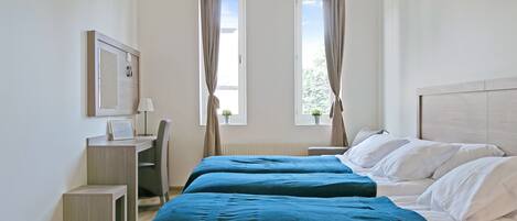 A hotel room with two beds, a desk, a chair, a small table, and a window with curtains.