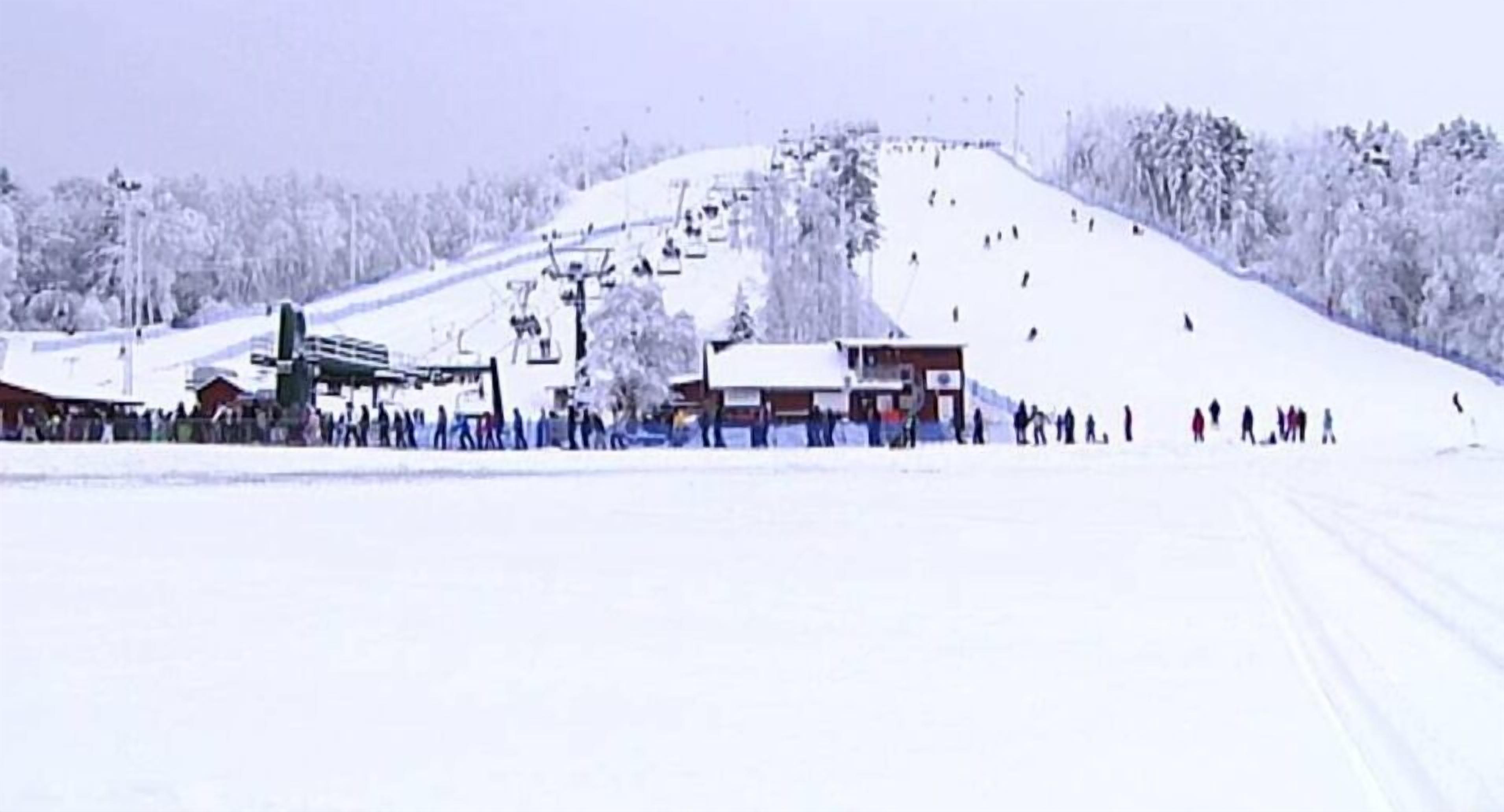 A snow-covered ski slope with a ski lift and a few buildings at the base.