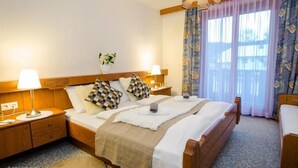 A hotel room with a double bed, two bedside tables with lamps, a small bedside table with a lamp, a window with patterned curtains, and a view of the outdoors. - Hotel Seelacherhof (Sankt Kanzian am Klopeiner See)