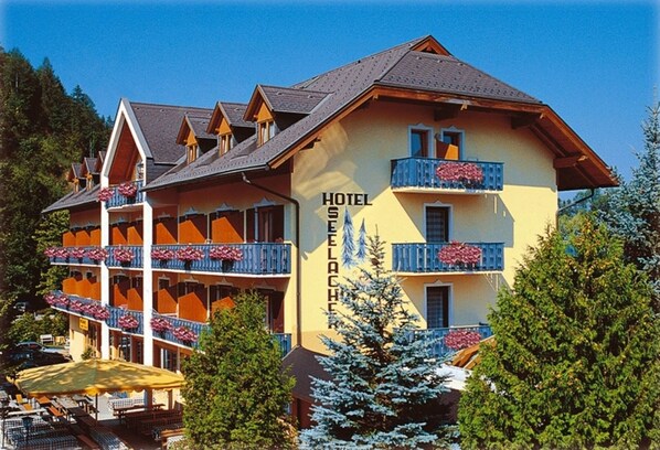 A multi-story hotel with balconies, a ski slope in the background, and a clear sky.