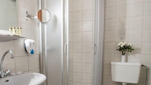 A bathroom with a sink, mirror, hand soap dispenser, toilet, and a shower enclosure. - Hotel Seelacherhof (Sankt Kanzian am Klopeiner See)