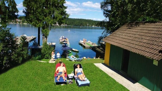 A lakeside property with a grassy lawn, a small building, and boats on the water. - Hotel Seelacherhof (Sankt Kanzian am Klopeiner See)