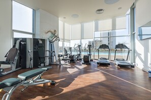 A modern gym with various exercise equipment, large windows, and a view of a swimming pool.