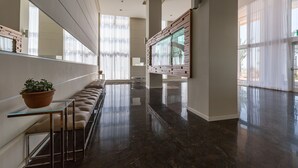 Un interior moderno con un largo banco, una mesa de vidrio y un amplio ventanal con cortinas translúcidas.