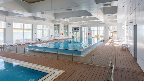 Una piscina interior con agua cristalina, rodeada de tumbonas y una terraza de madera.