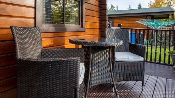 A wooden cabin with wicker furniture on a deck. - The Steadings (Cupar)