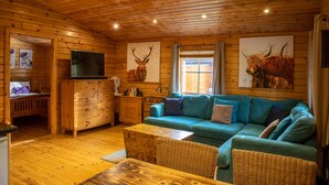 A wooden cabin interior with a sofa, a wooden dresser, a television, and artwork on the walls. - The Steadings (Cupar)