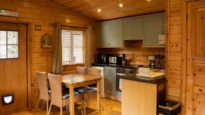 A wooden cabin interior with a dining area, kitchen, and a small island counter. - The Steadings (Cupar)