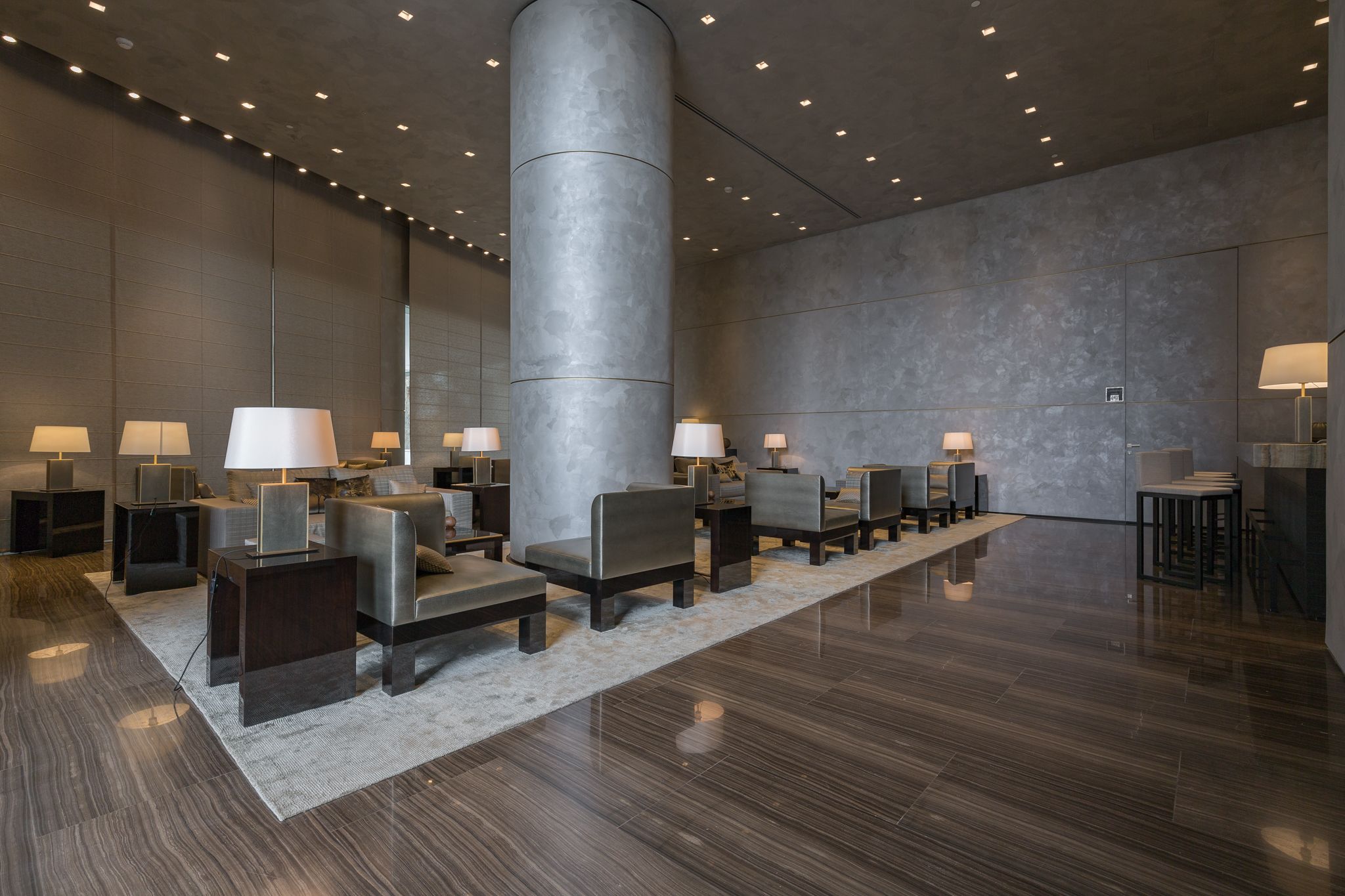 Um lobby moderno com uma coluna central, várias áreas de estar e mesas com abajures.