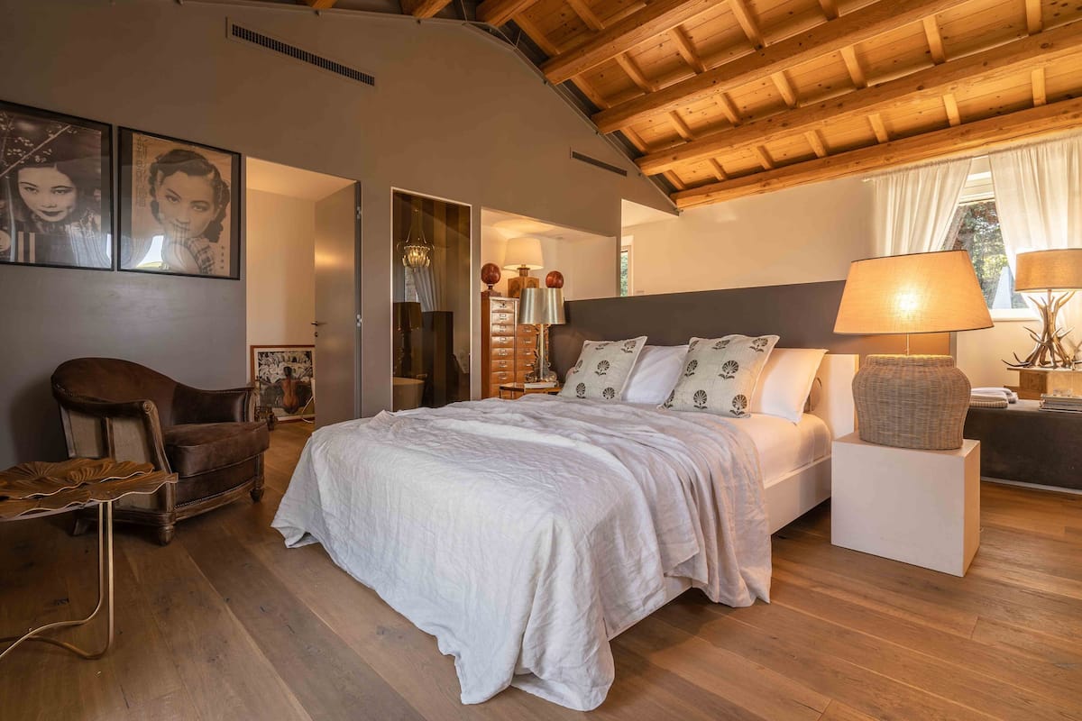 Une chambre à coucher avec un grand lit, un plafond en bois, une chaise et une table de chevet avec une lampe.