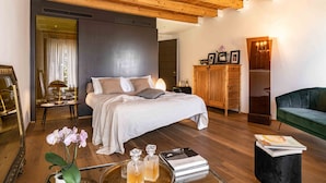 Une chambre moderne avec un grand lit, un plafond en bois, un canapé vert et une petite table sur laquelle sont posés des livres et des fleurs.