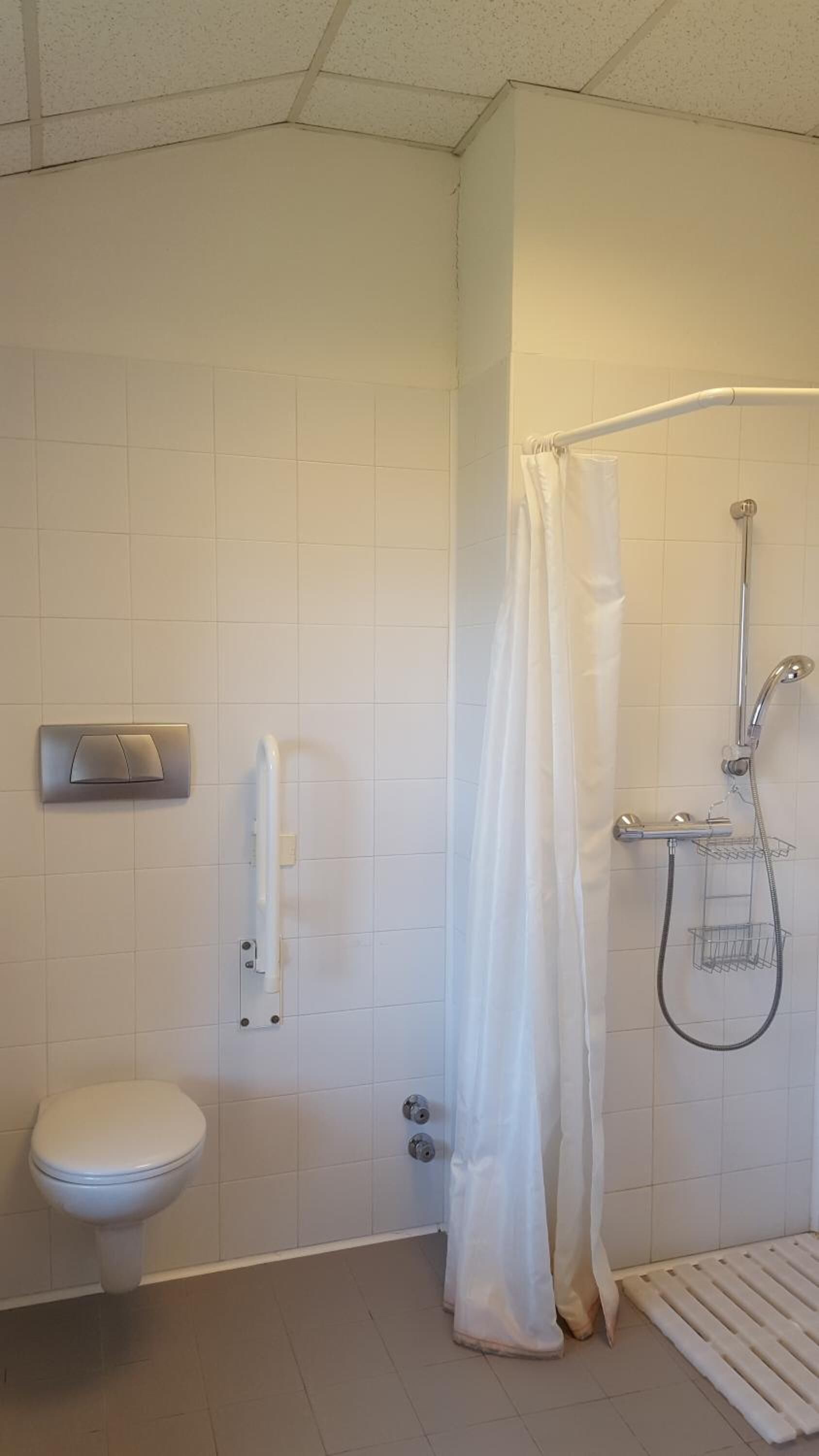 Un baño con inodoro, ducha con cortina y un perchero para toallas.
