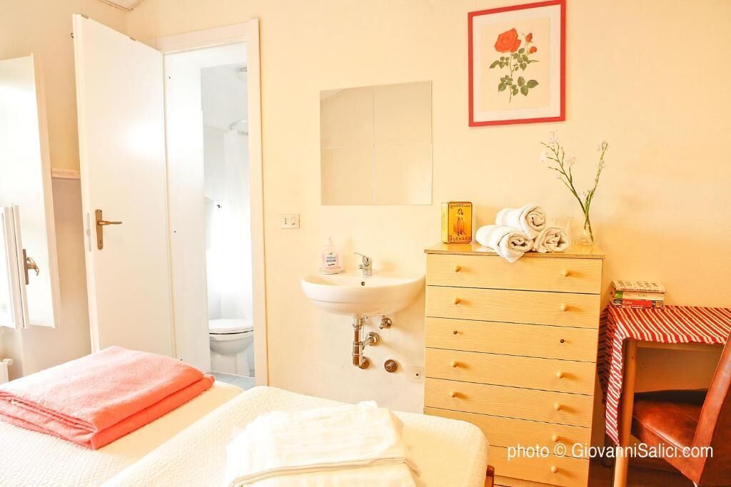 Une chambre d’hôtel avec un lit, une commode en bois, un lavabo et un tableau encadré au mur.