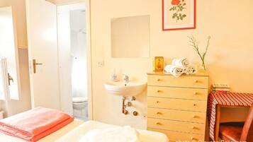 Une chambre d’hôtel avec un lit, une commode en bois, un lavabo et un tableau encadré au mur.