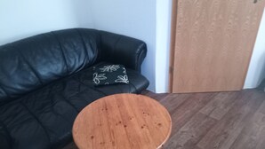 A room with a black leather sofa, a small wooden stool, and a wooden door. - Hotel zur Tanne (Zwickau)