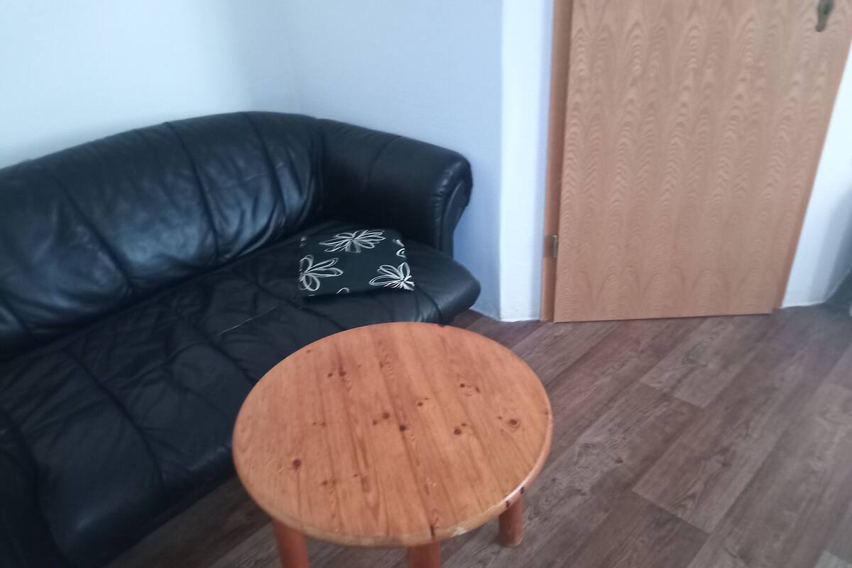 A room with a black leather sofa, a small wooden stool, and a wooden door.