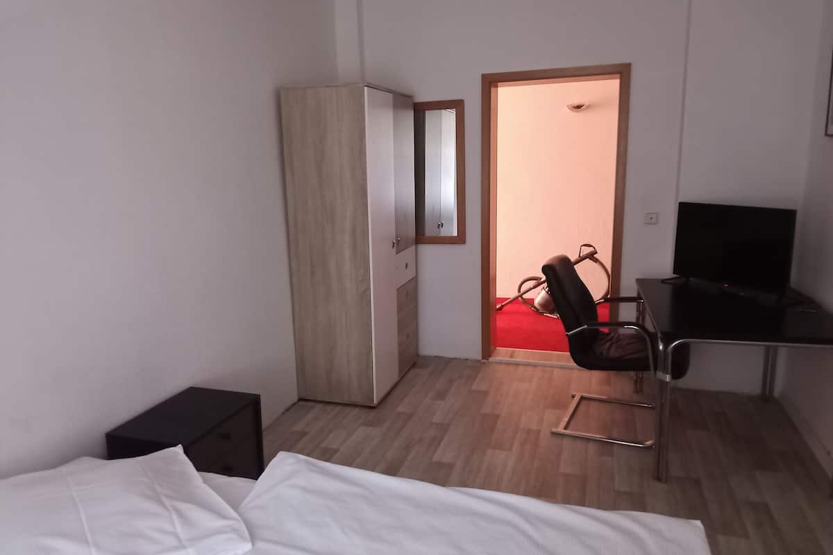 A hotel room with a bed, a desk with a chair, a wardrobe, and a television.