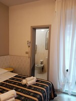 A hotel room with a bed, a bathroom visible through a doorway, and a window with curtains.