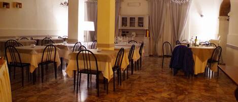 Zona pranzo con diversi tavoli e sedie, un lampadario e un pavimento in marmo.