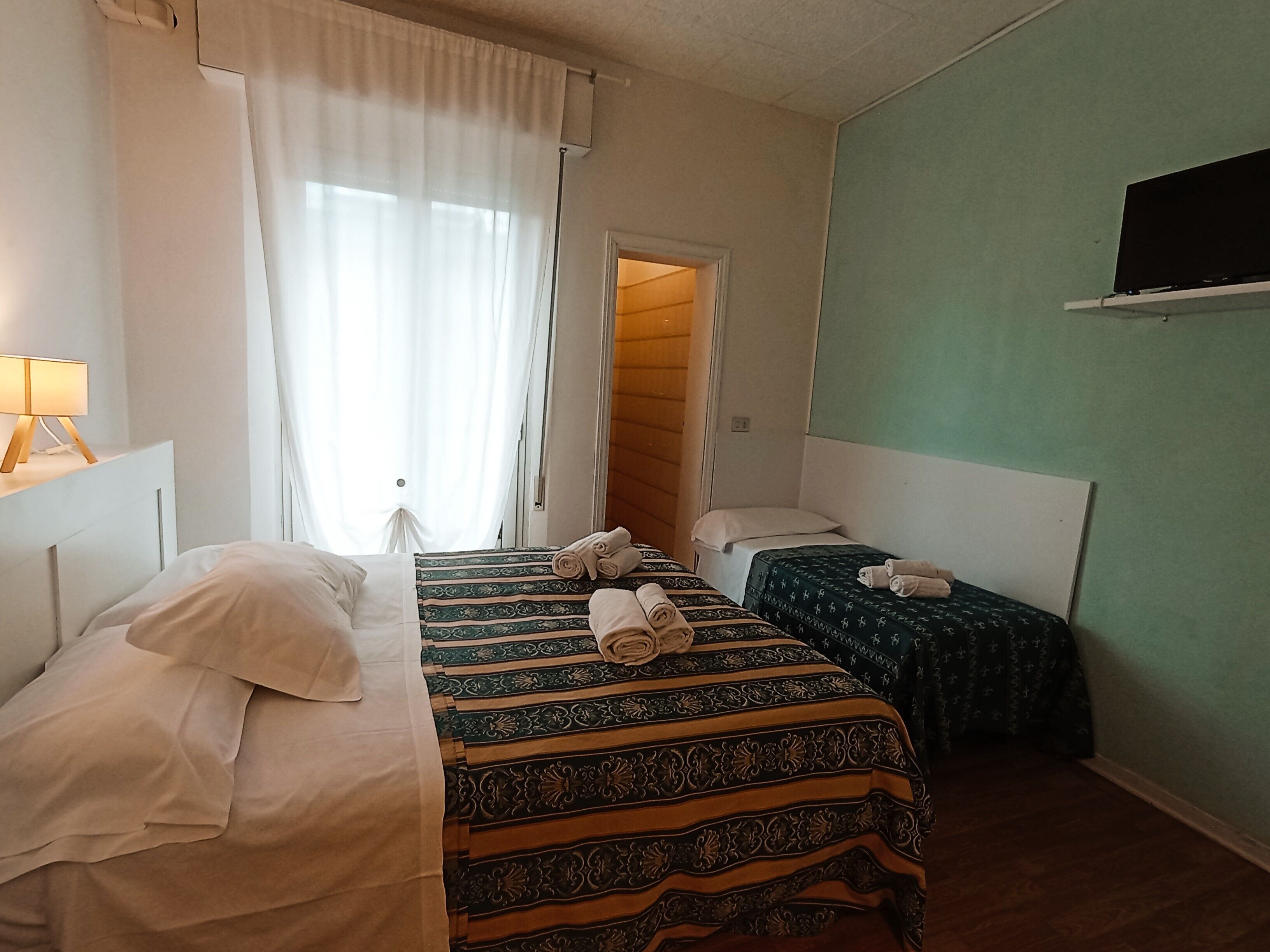 A hotel room with two beds, a television on the wall, and a window with curtains.