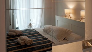 A hotel room with a bed, a mirror, a bedside table with a lamp, and a window with curtains.