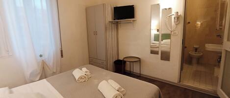 Ein Hotelzimmer mit Bett, Fernseher, Spiegel, Bad mit Toilette und Waschbecken sowie einem kleinen Tisch.