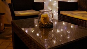 A room with wicker furniture, a glass table with a candle, and string lights on the wall.