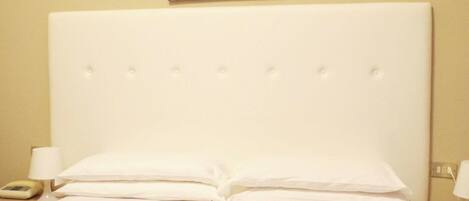 Una habitación de hotel con una cama que tiene una colcha a rayas, dos toallas enrolladas, un cabecero blanco y un cuadro en la pared.