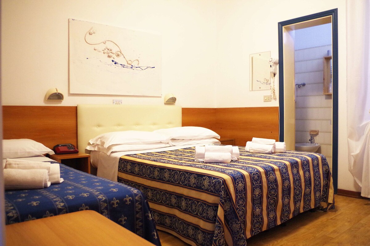 Hotellihuone, jossa on kaksi sänkyä, puinen pääty, yöpöytä, jossa on puhelin, ja seinälle kiinnitetty taideteos.