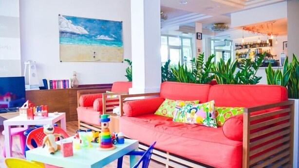 A bright living room with a red sofa, a painting of a beach, and a bar area with plants.