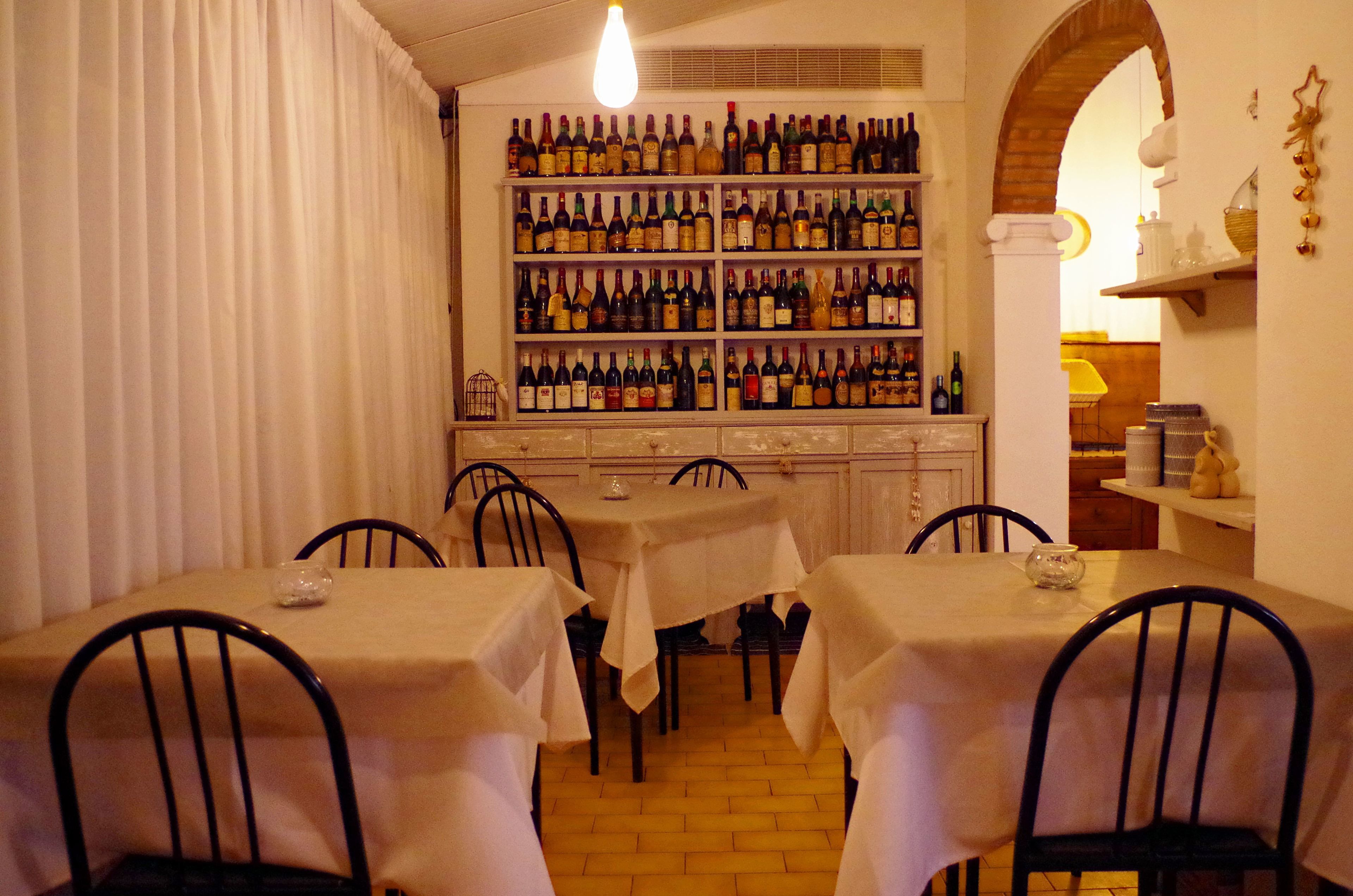 Uma sala de jantar com mesas cobertas por toalhas brancas, cadeiras e uma parede com garrafas de vinho.
