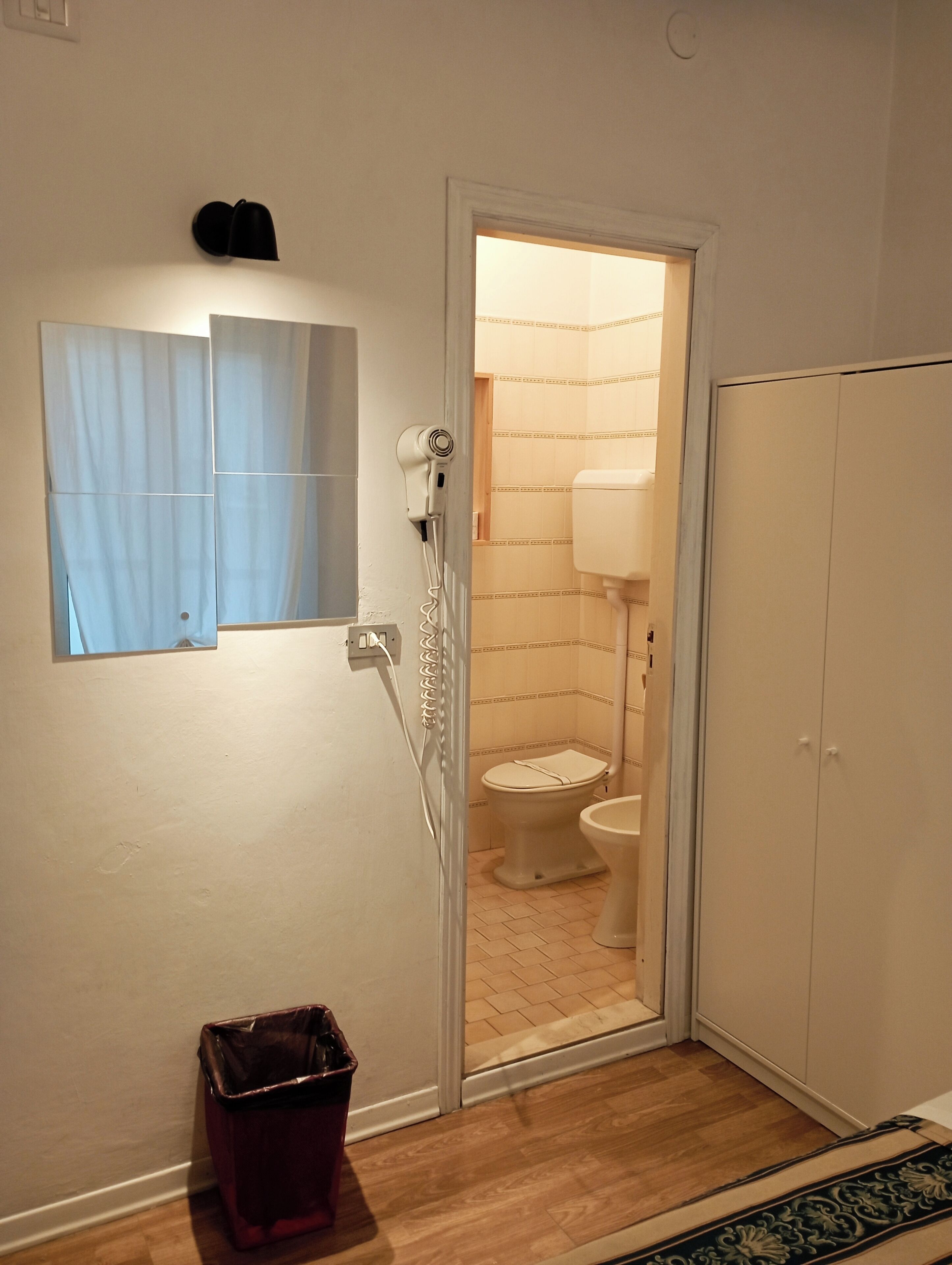 A bathroom with a toilet, a hairdryer, and a trash bin.