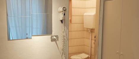 A bathroom with a toilet, a hairdryer, and a trash bin.