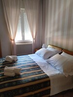 Una habitación de hotel con una cama, dos almohadas, una mesita de noche y una ventana con cortinas.