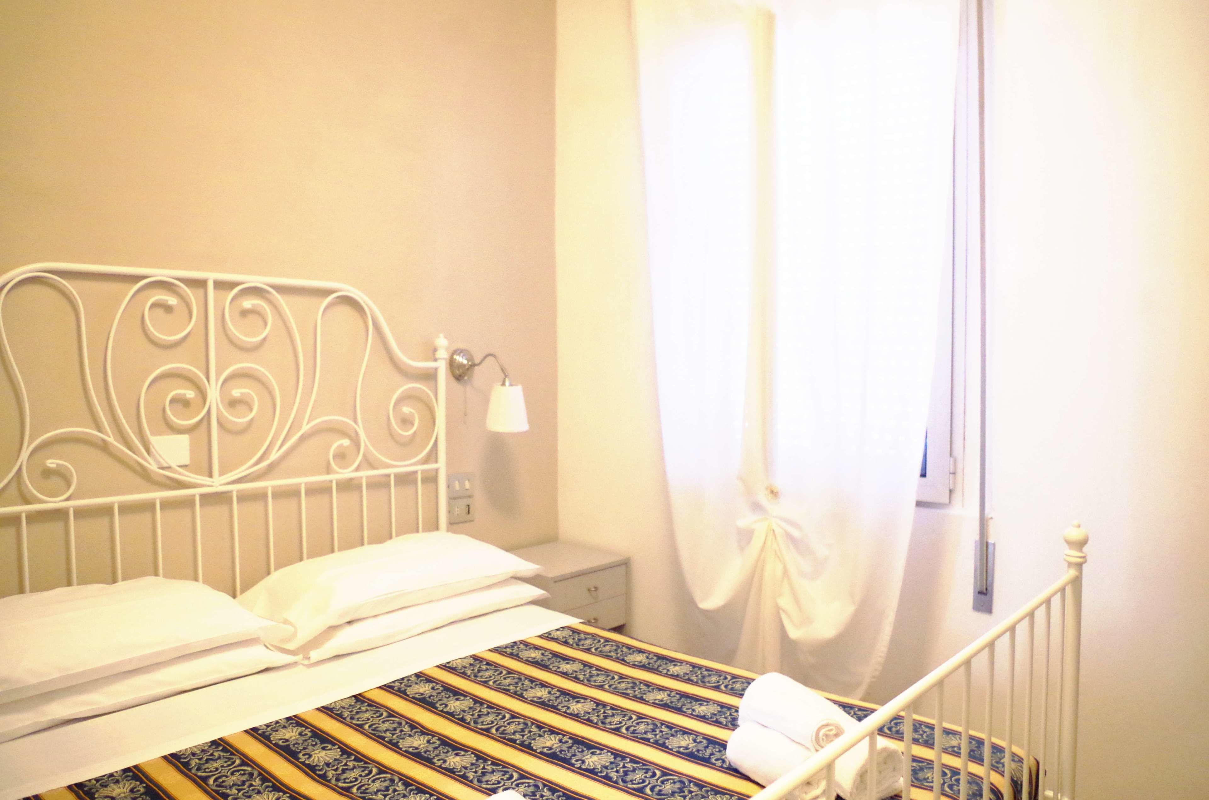 A bed with a metal headboard, a bedside table, a nightstand, and a curtain.