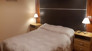 A bedroom with a large bed, wooden headboard, two bedside tables with lamps, and a small picture on the wall. - Apart El Nevado (Malargüe)