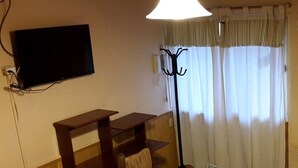 A room with a television mounted on the wall, a wooden bench, a floor lamp, and a window with curtains. - Apart El Nevado (Malargüe)