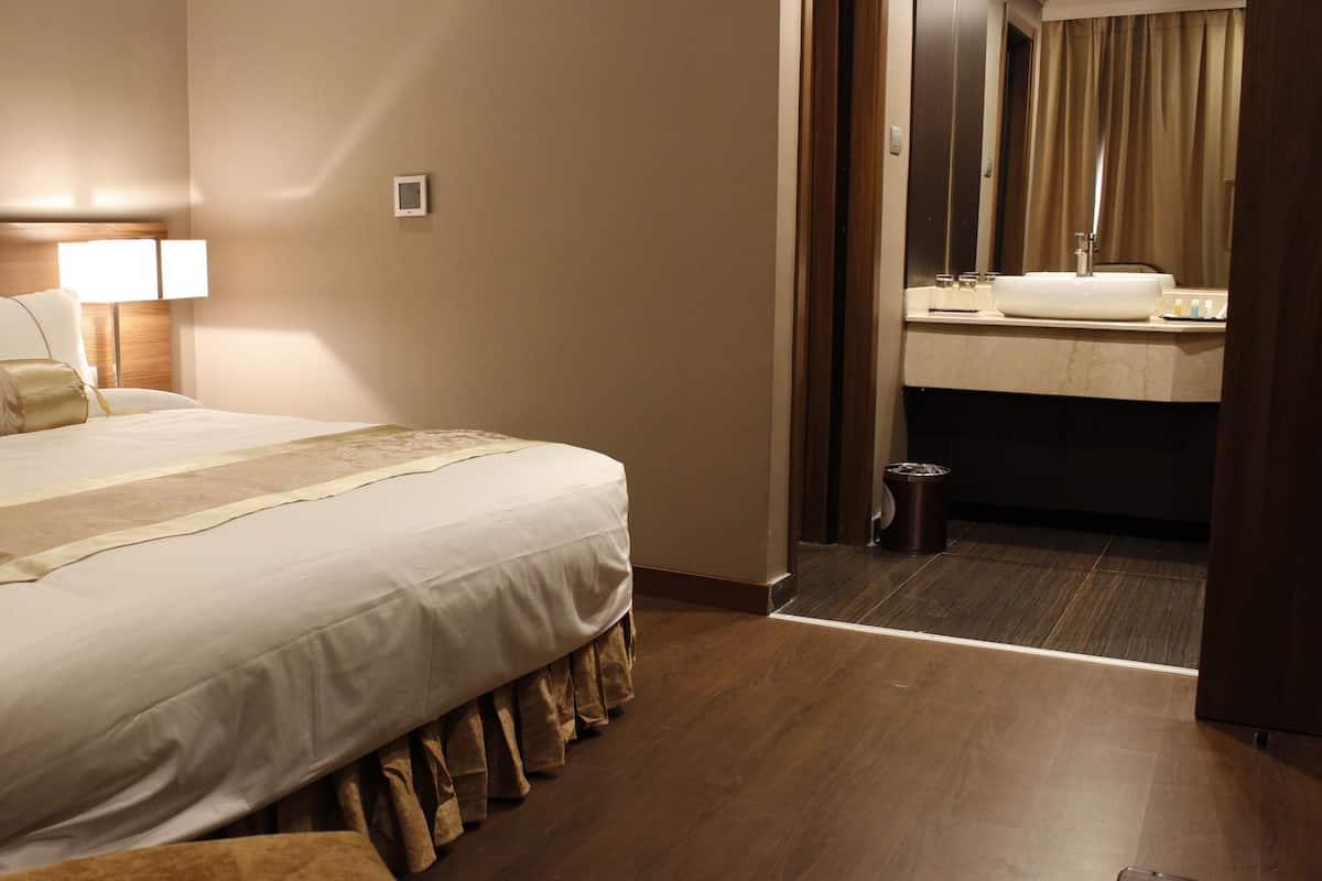 A hotel room with a neatly made bed, a bedside lamp, a small bedside table, and a view into the bathroom through an open door.