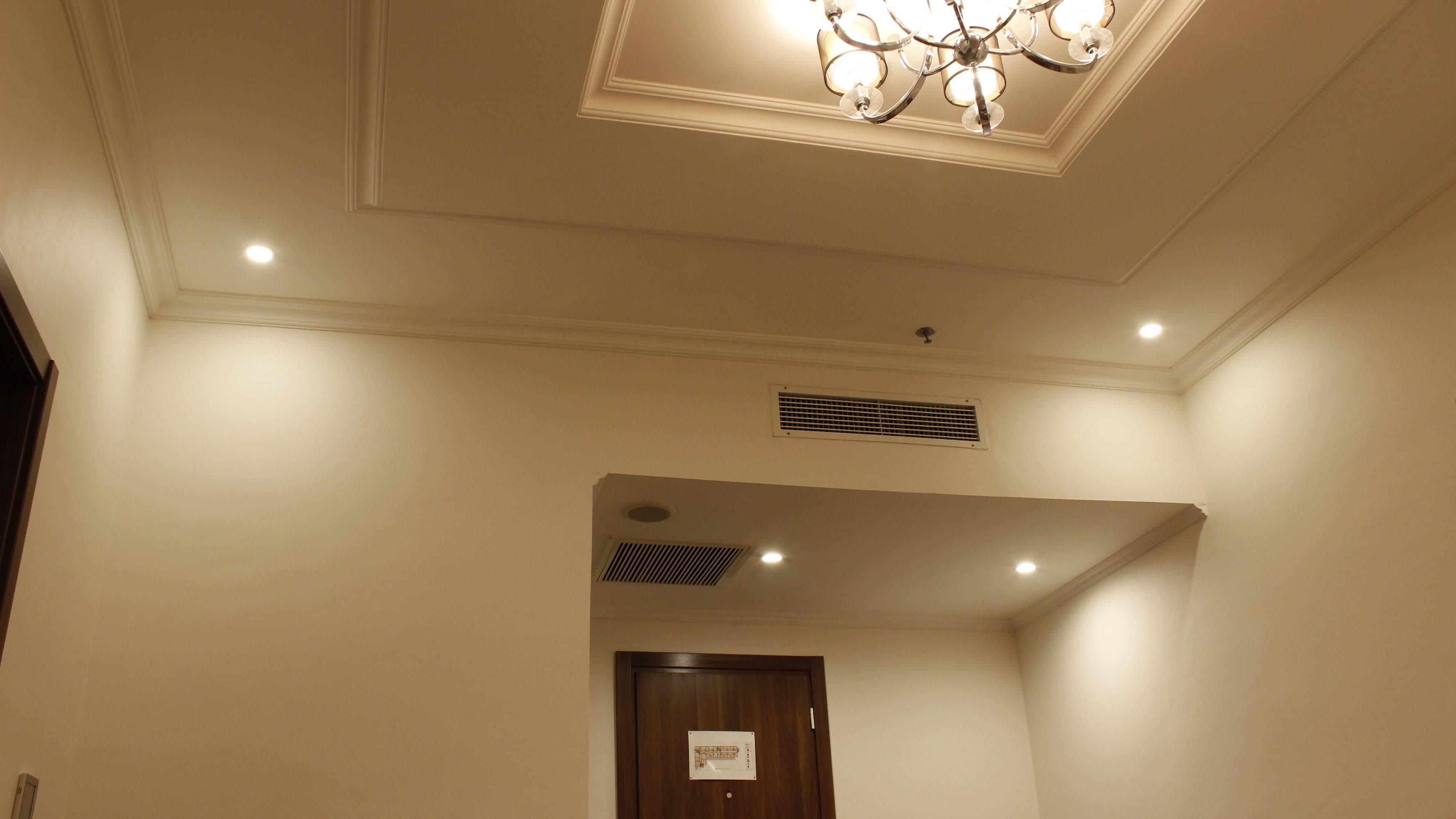 A hotel hallway with a chandelier, recessed lighting, a vent, and a door with a sign.