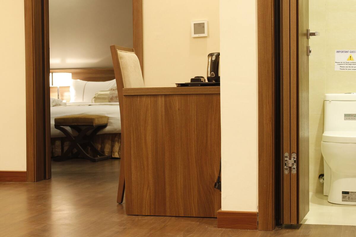 A hotel room with a wooden desk, a bed, and a nightstand.